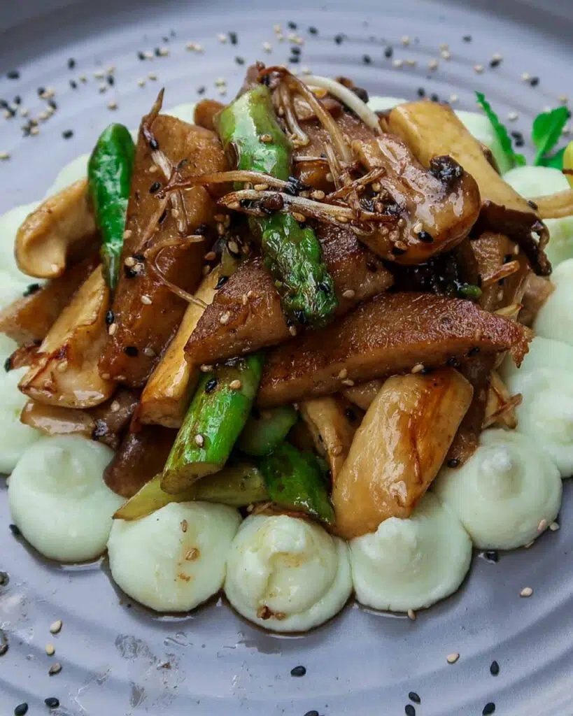 A mushroom and asparagus stir fry with piped mashed potato surrounding it