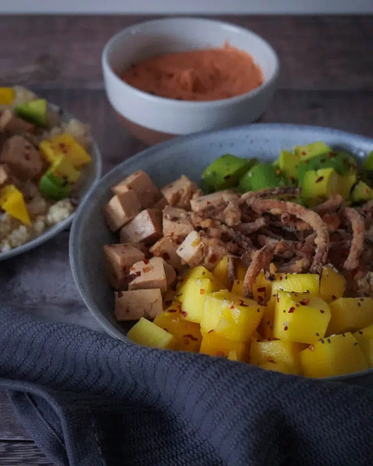 A bowl of vegan food including mango cubes, avocado, crispy fried onions, marinated tofu and quinoa