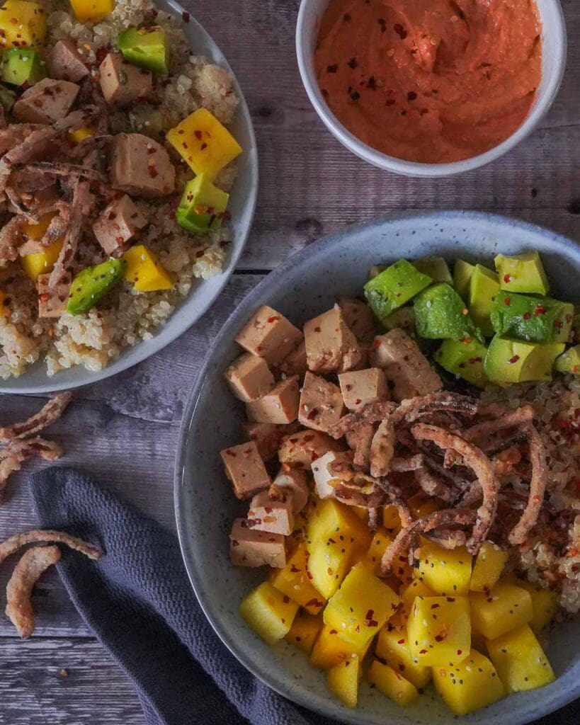 A bowl of vegan food including mango cubes, avocado, crispy fried onions, marinated tofu and quinoa