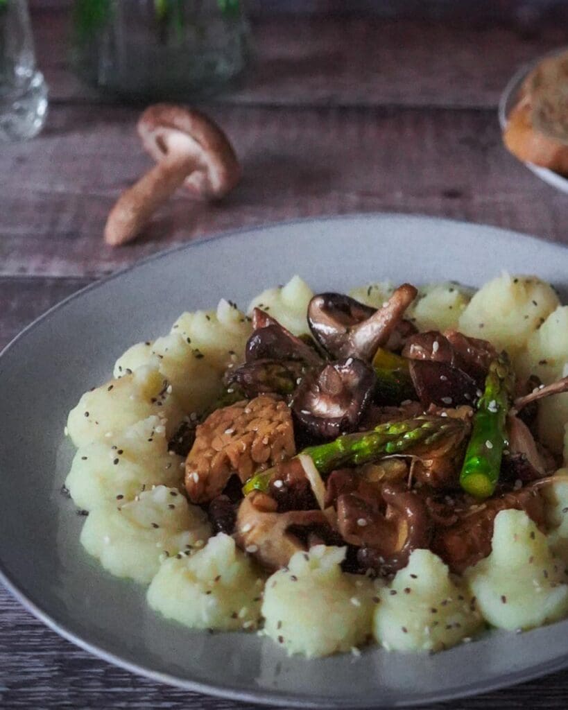 A wild mushroom and asparagus stir fry on a plate with mashed potato piped around it