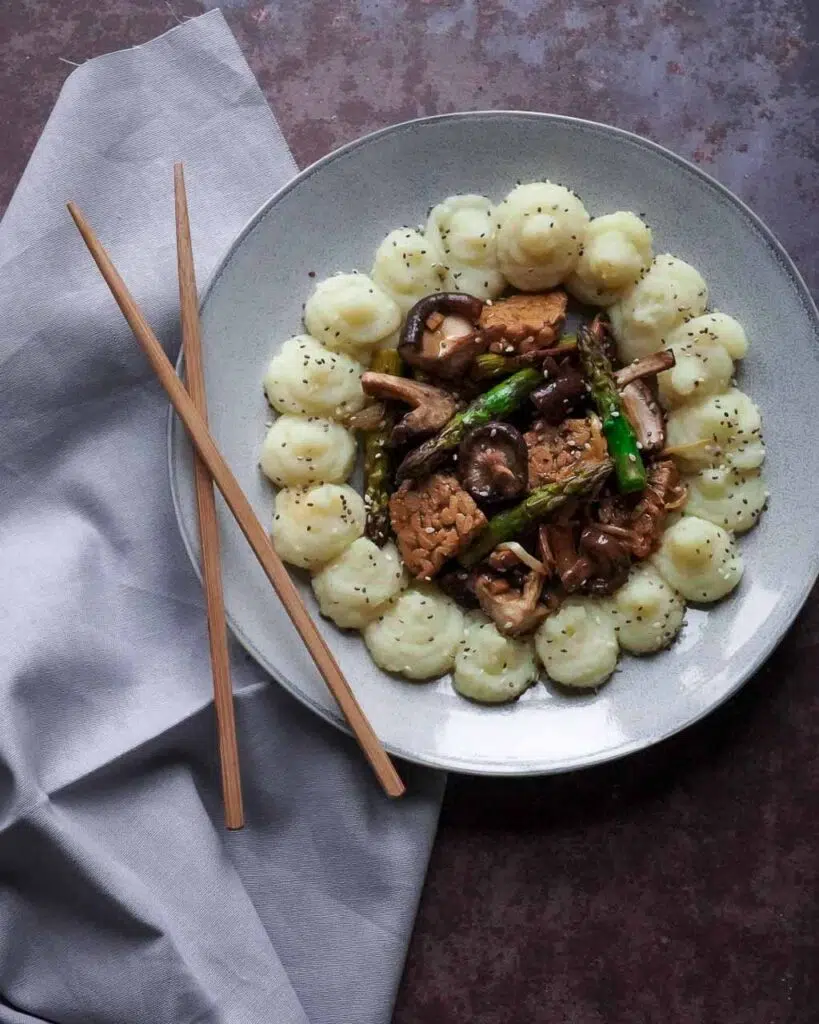 A wild mushroom and asparagus stir fry on a plate with mashed potato piped around it