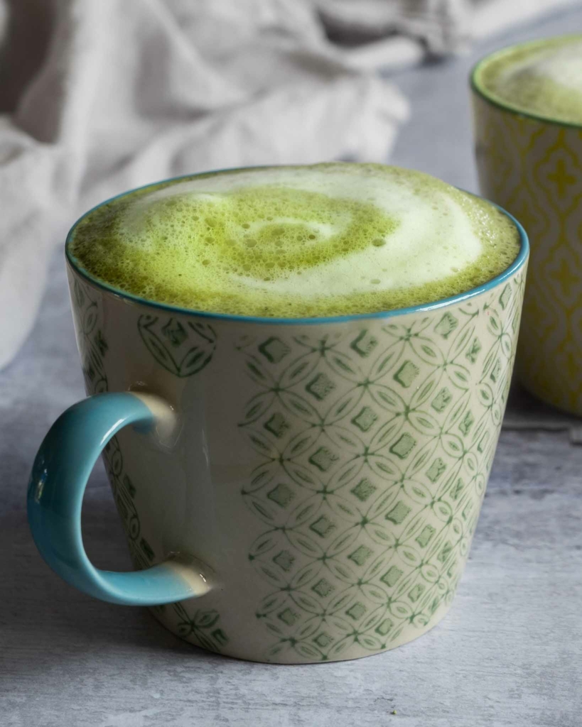 A close up photo of a cup of vibrant green matcha latte with frothy oat milk on top