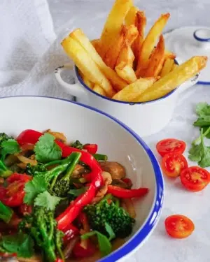 A colourful vegan lomo saltado stir fry with green and red vegetables, accompanied by crispy oven cooked chips
