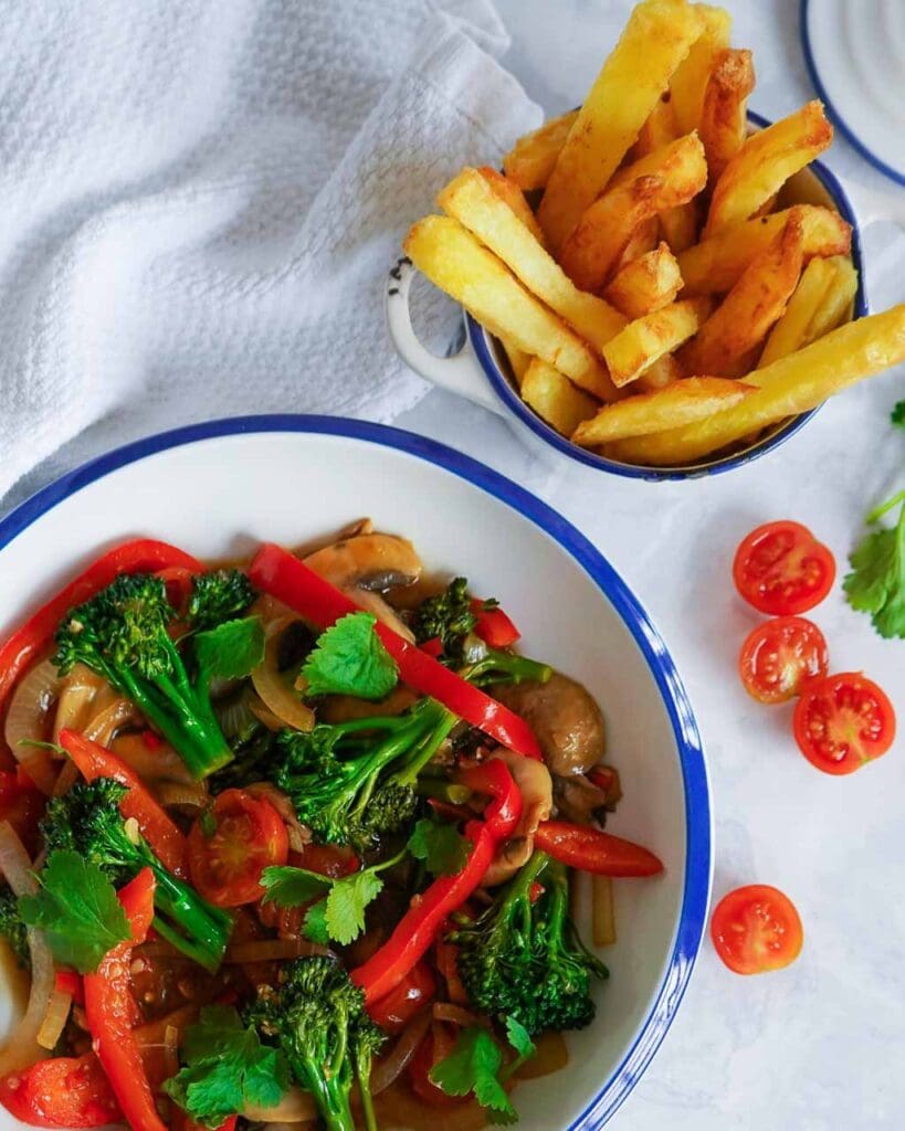 A colourful vegan lomo saltado stir fry with green and red vegetables, accompanied by crispy oven cooked chips