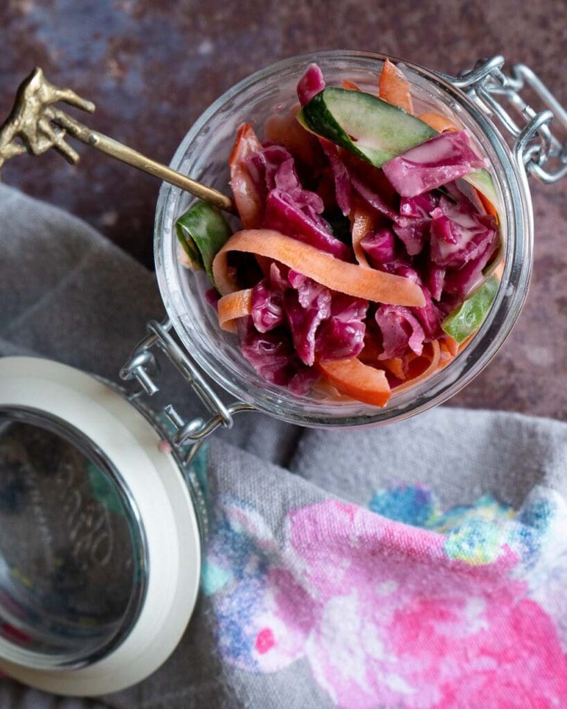 A glass jar of rainbow vegetable ribbons in a vegan slaw