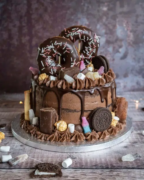 A vegan chocolate cake stacked high with naked chocolate frosting, a chocolate drizzle, chocolate doughnuts, sweets, biscuits and chocolate bars