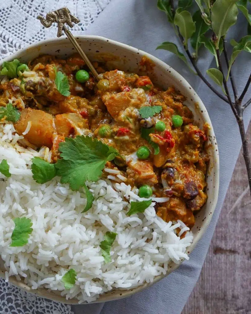 A bowl of vegan slow cooker vegetable korma curry with white rice and a sprinkling of fresh coriander