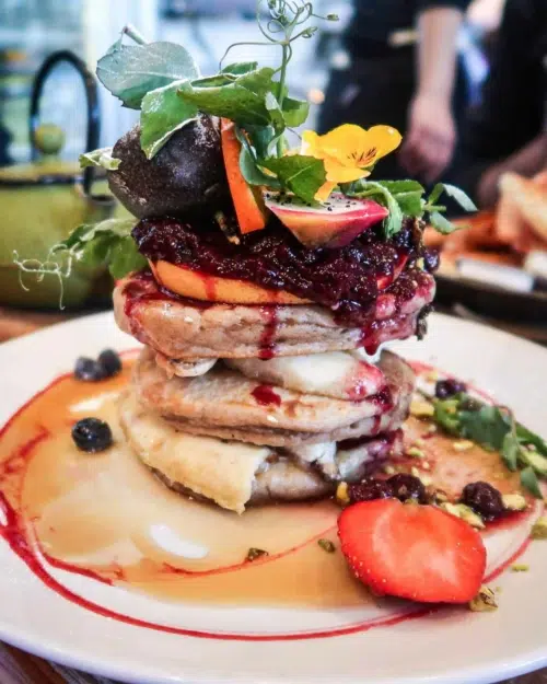 A beautiful and colourful stack of vegan pancakes with fresh berries, maple syrup, edible flowers, dragon fruit and passion fruit