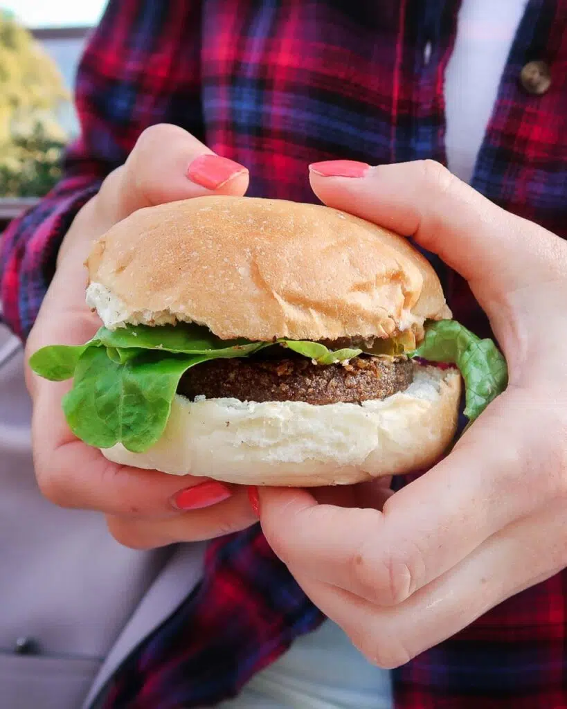 Woman holding a mini vegan burger in a bun with lettuce spilling out