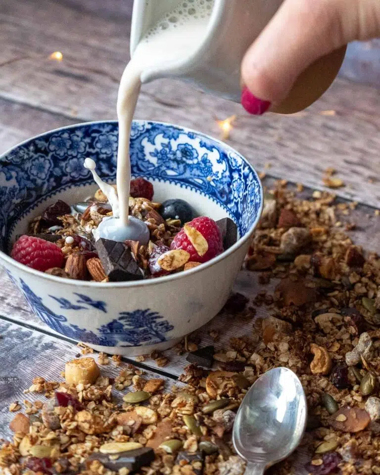 A bowl of healthy vegan granola with chocolate and berries, having vegan milk poured on top
