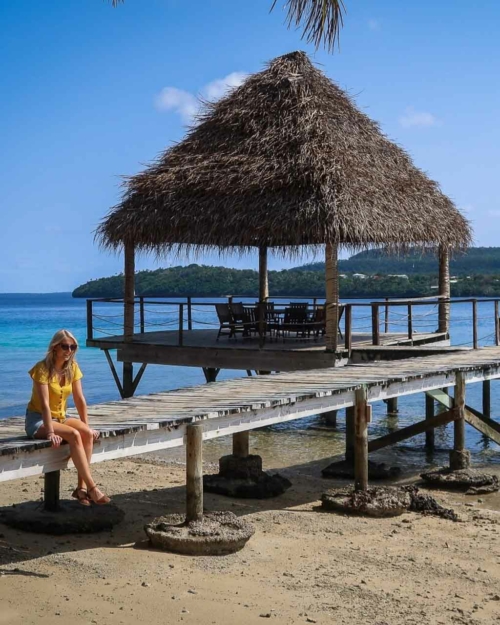 A woman in a yellow top sat on a boat jetty on a beach in Vav'au Tonga overlooking the blue ocean