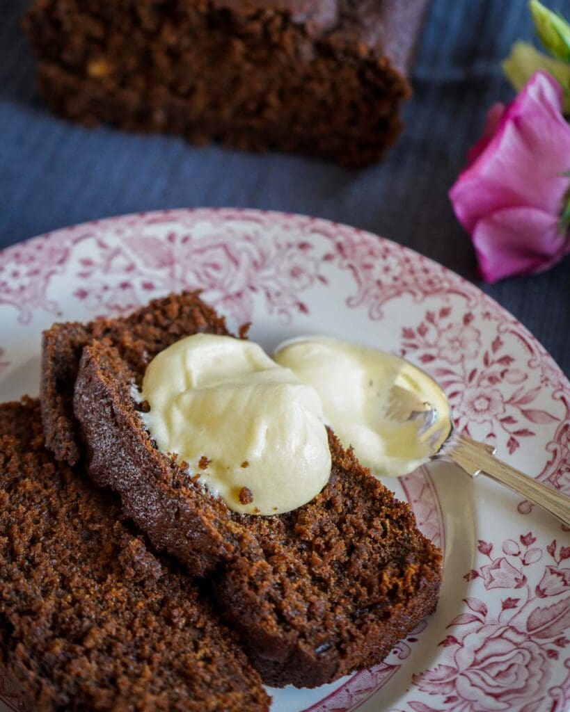 Two slices of moist vegan ginger cake on a pretty pink and white plate, with a dollop of passion fruit icing on top