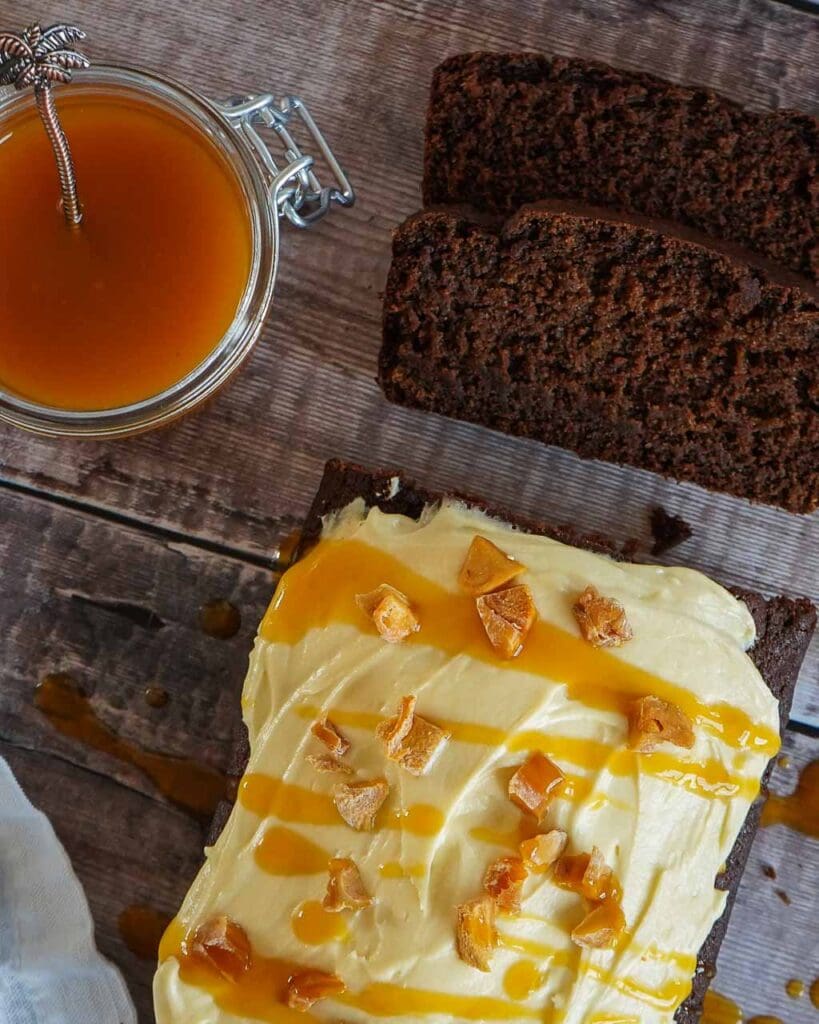 A vegan Jamaican ginger cake on a wooden bench, covered in passion fruit icing with a drizzle of passion fruit coulis
