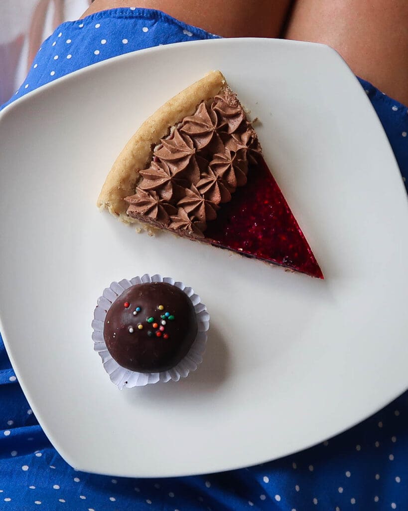 A vegan raspberry jam tart and chocolate snack ball on a white plate