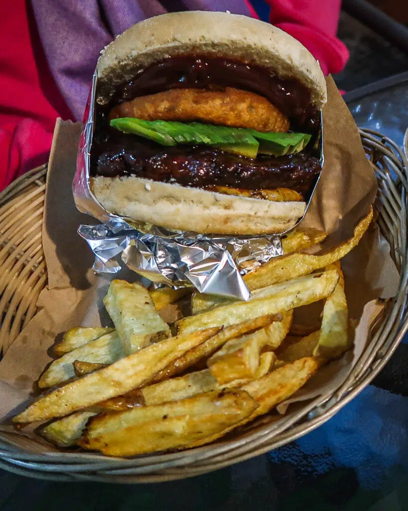 A dirty vegan burger wrapped in foil with rustic fries, served in a wicker basket, from a vegan restaurant in Santiago, Chile