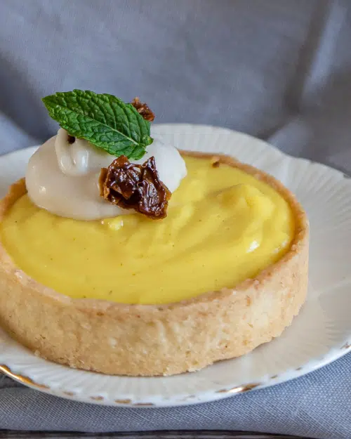 A pretty lemon curd pie in a golden pastry case, topped with whipped coconut cream, candied coconut and a fresh mint leaf