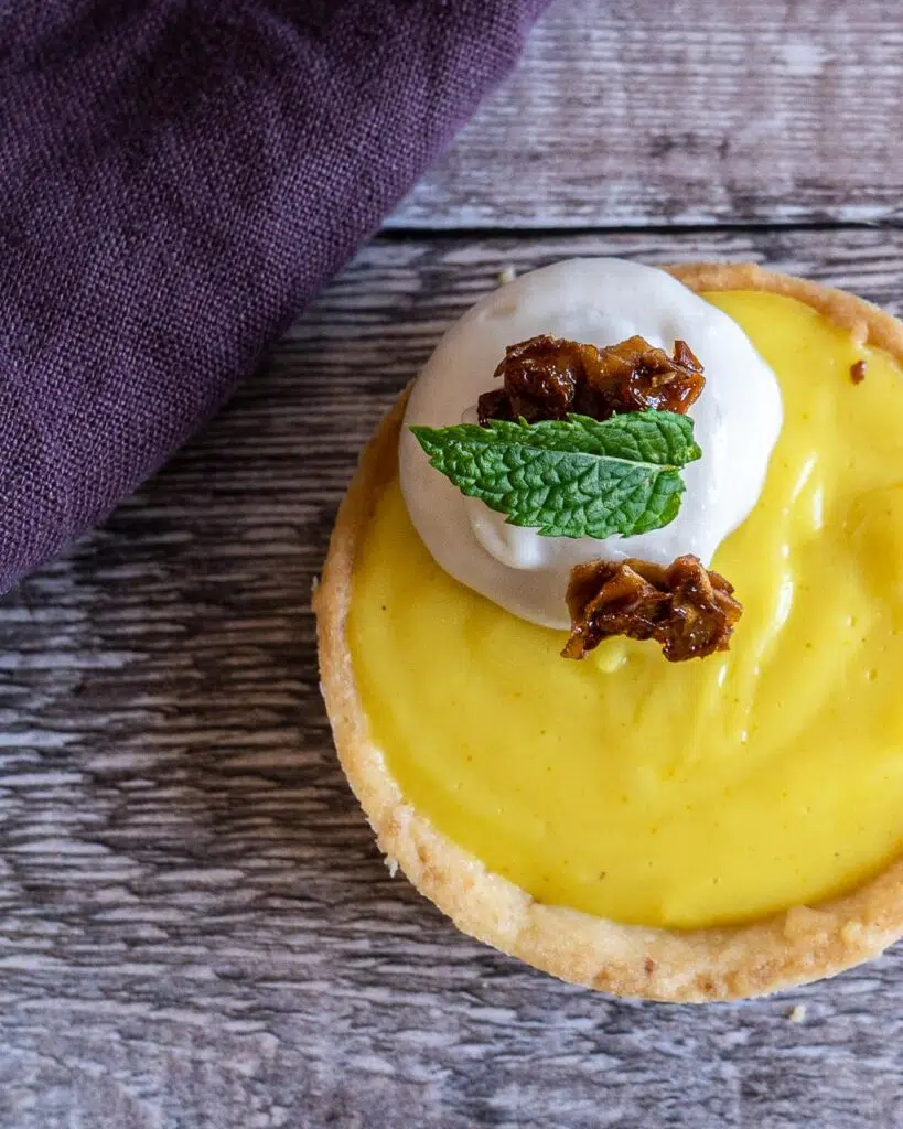 A pretty lemon curd pie in a golden pastry case, topped with whipped coconut cream, candied coconut and a fresh mint leaf