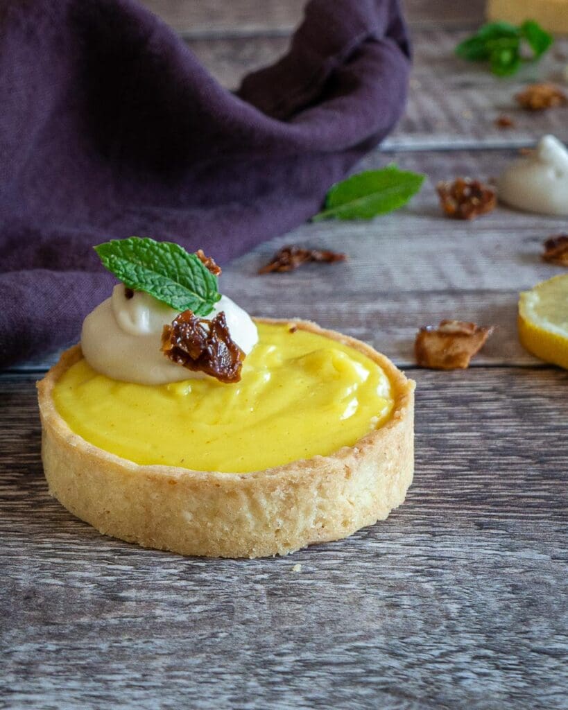 A pretty lemon curd pie in a golden pastry case, topped with whipped coconut cream, candied coconut and a fresh mint leaf