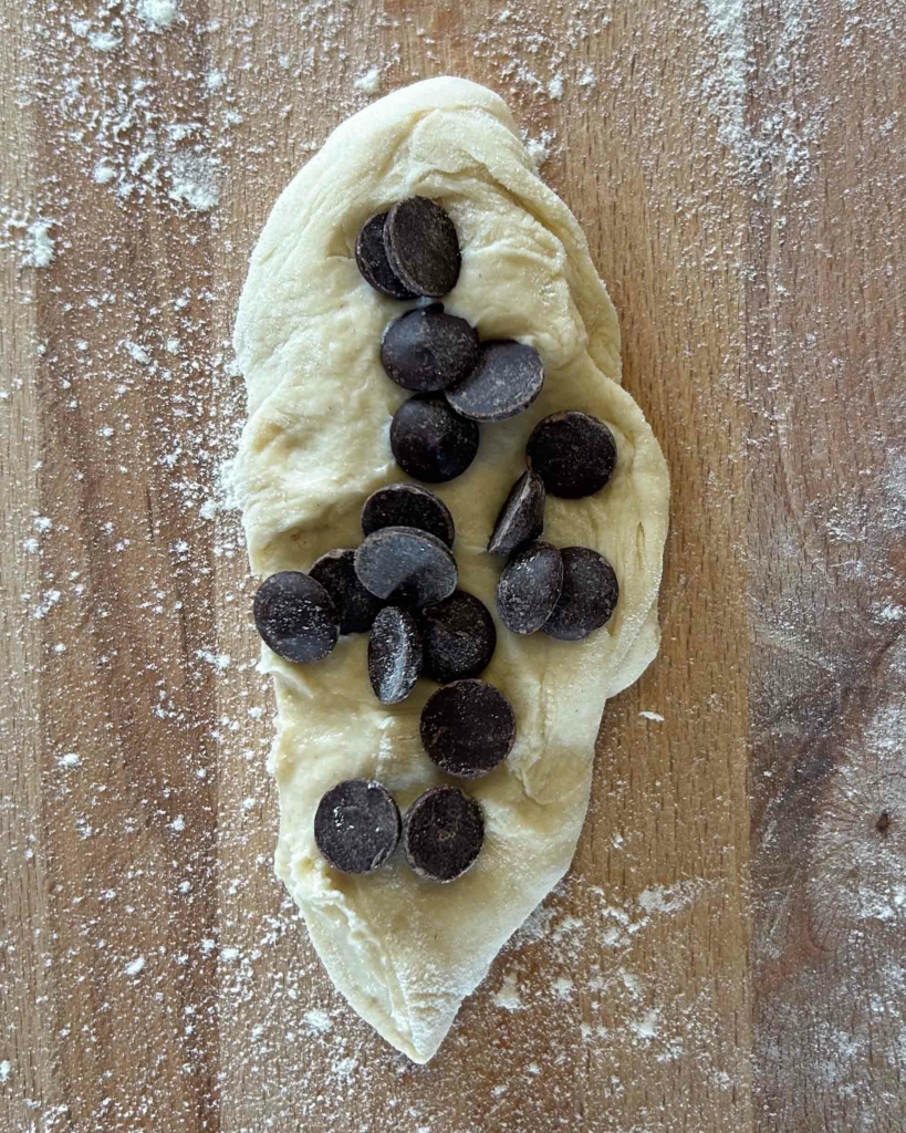 A piece of dough flattened, with chocolate chips placed on top ready to be folded in