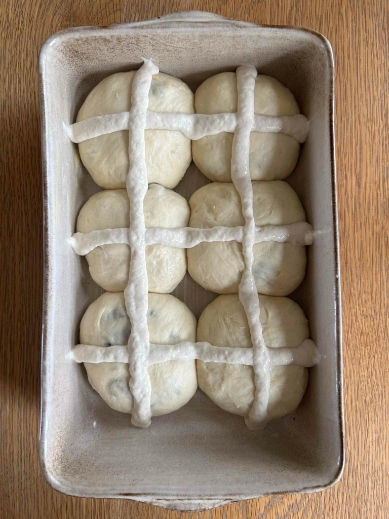 Vegan chocolate chip hot cross buns in a baking dish, with crosses piped on, ready to go in the oven