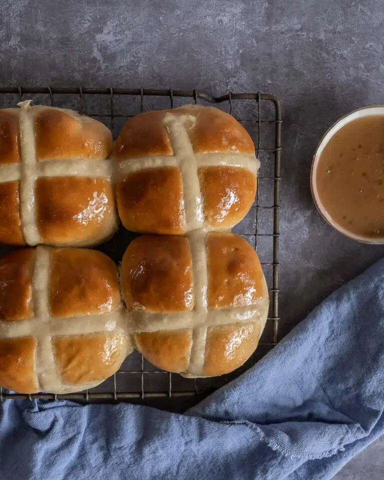 Squishy vegan hot cross buns on a cooling rack next to a bowl of salted caramel dipping sauce