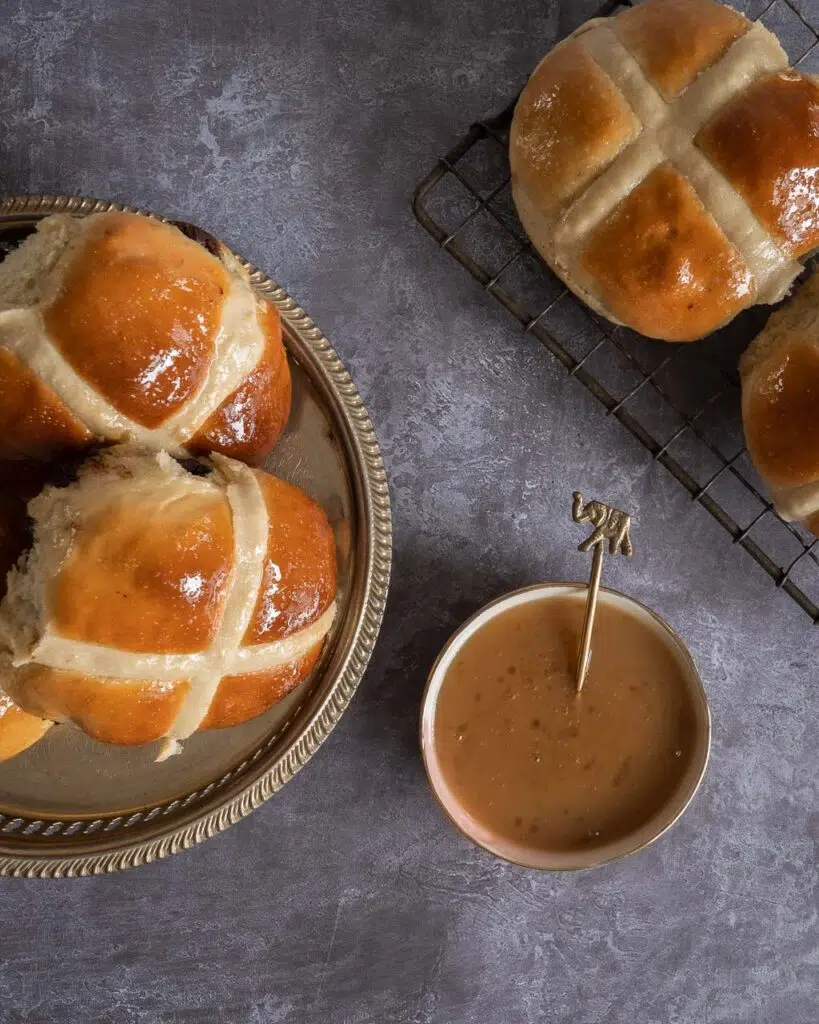 Soft vegan hot cross buns on a tray next to a bowl of salted caramel dipping sauce