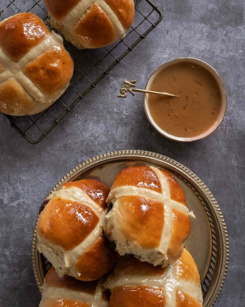 A tray of vegan chocolate chip hot cross buns next to a small bowl of vegan salted caramel sauce.