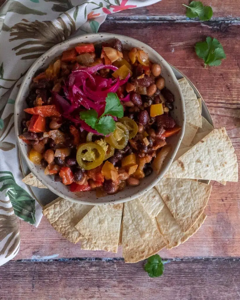 A bowl of black bean chilli with pickled red onions and jalapeño slices