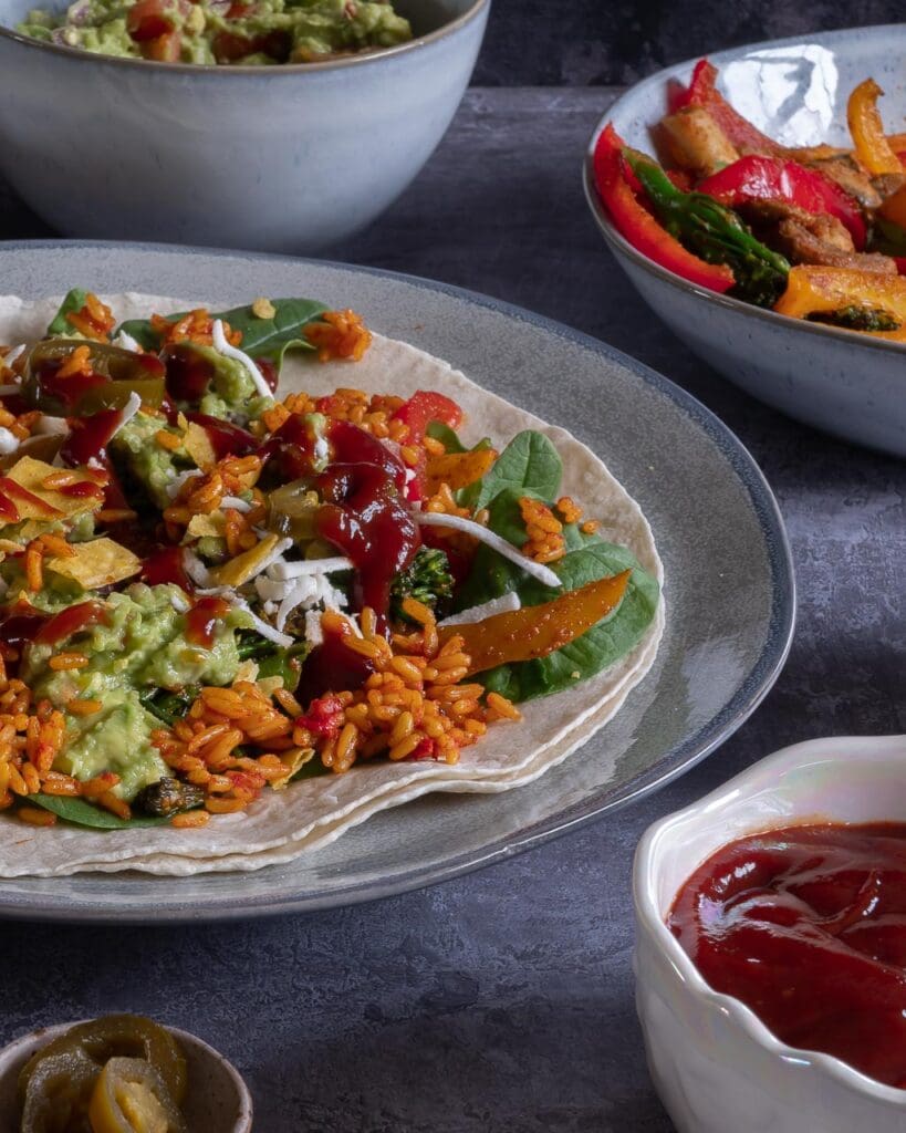 Close up of a vegan burrito in the making, with spicy rice, fajita vegetables, guacamole, chipotle sauce and crumbled tortilla chips