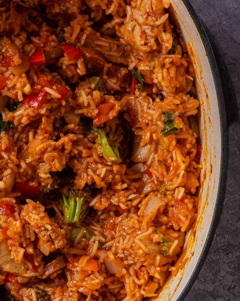 A large cast iron pan filled with colourful vegan jambalaya, showing fresh veggies and vegan chicken
