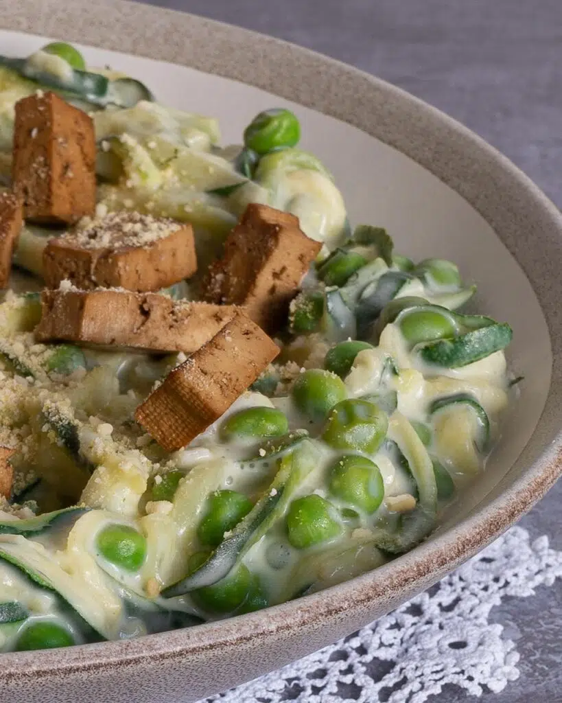 Close up of a bowl of healthy vegan carbonara made with zoodles in a creamy sauce, topped with smokey tofu bacon and vegan parmesan
