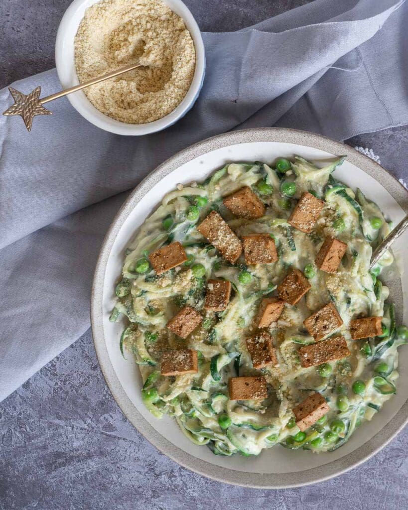 Overhead shot of a bowl of healthy vegan carbonara made with zoodles in a creamy sauce, topped with smokey tofu bacon and vegan parmesan