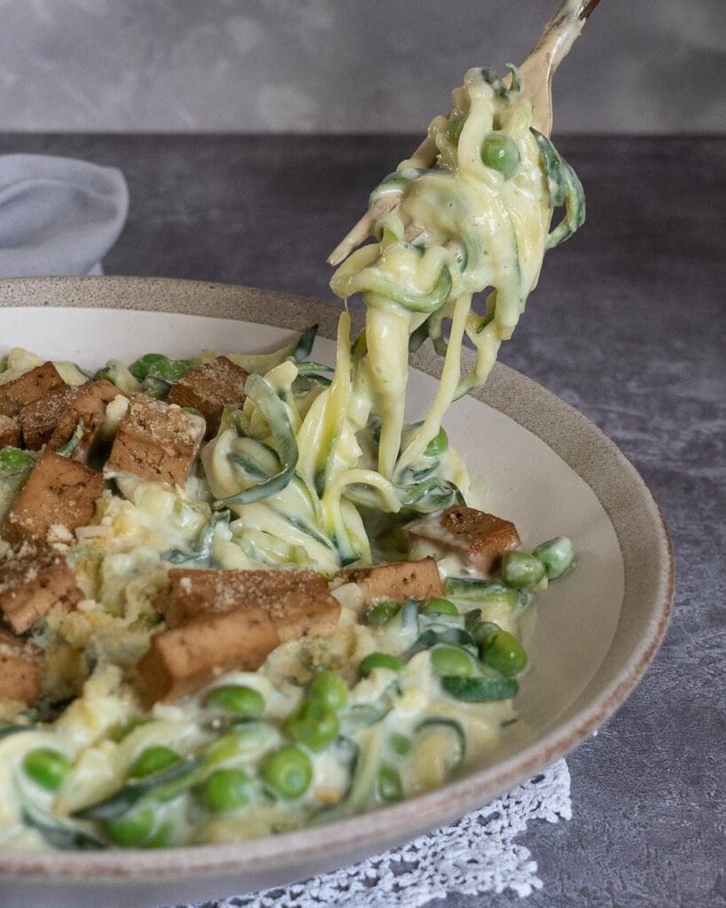 A bowl of healthy vegan carbonara made with spiralised courgette in a creamy sauce, topped with smokey tofu bacon and vegan parmesan