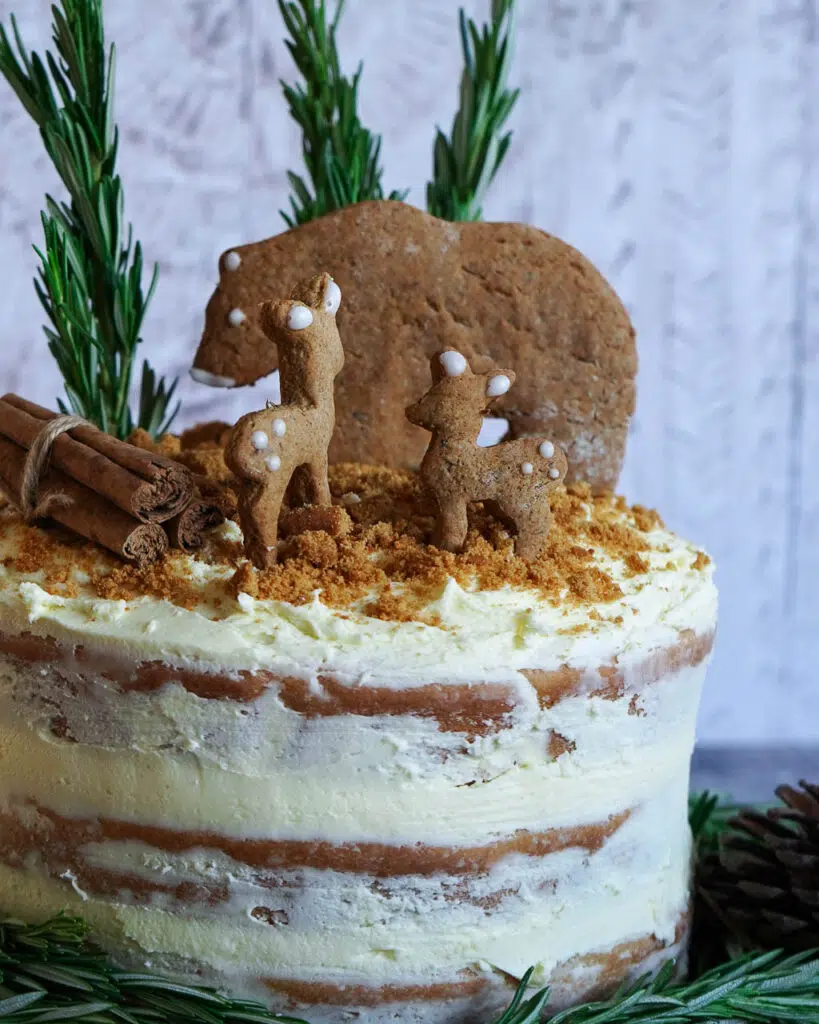 A layered vegan lemon cake with lemon naked frosting, decorated with a gingerbread bear and deer on top with rosemary trees