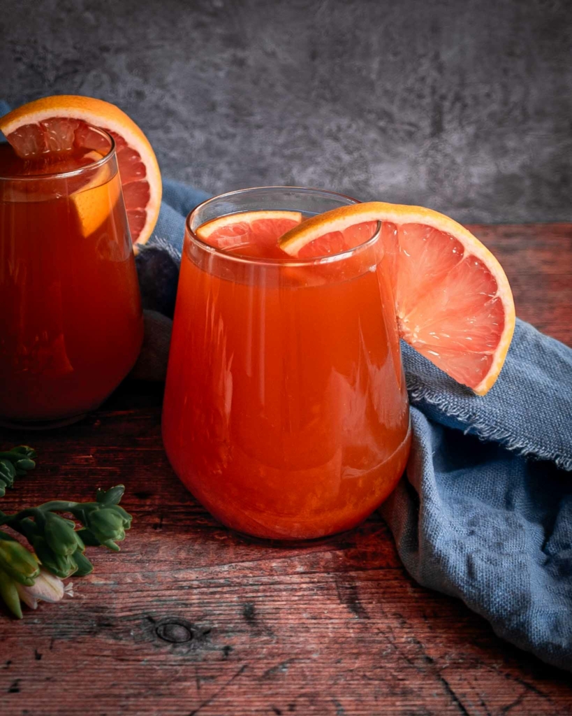 A vibrant orange glass of pink grapefruit kombucha sat on a rustic wooden tabletop