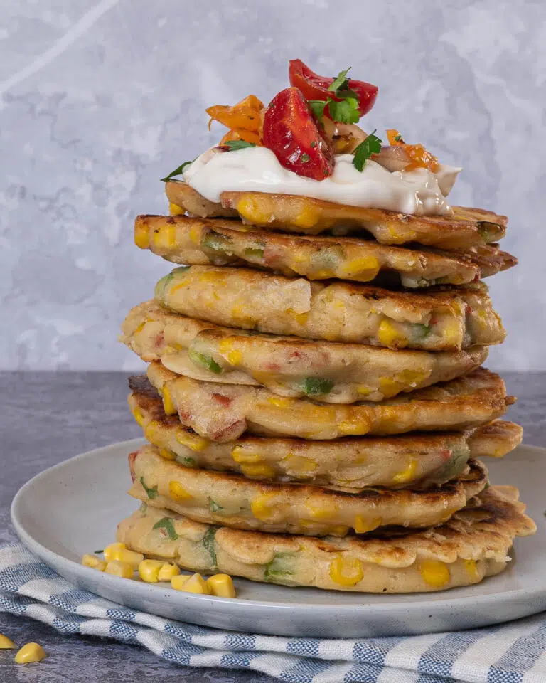 A stack of vegan sweetcorn fritters topped with dairy free creme fraiche and chipotle salsa