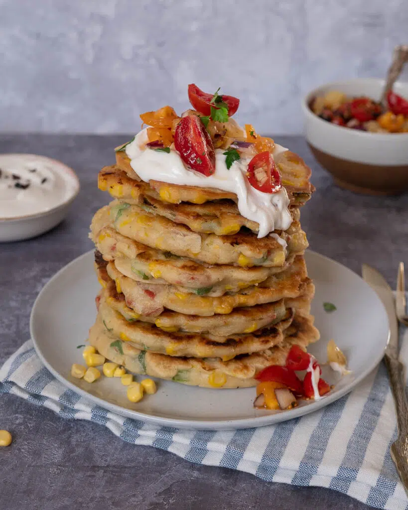 A stack of vegan sweetcorn fritters topped with dairy free creme fraiche and chipotle salsa