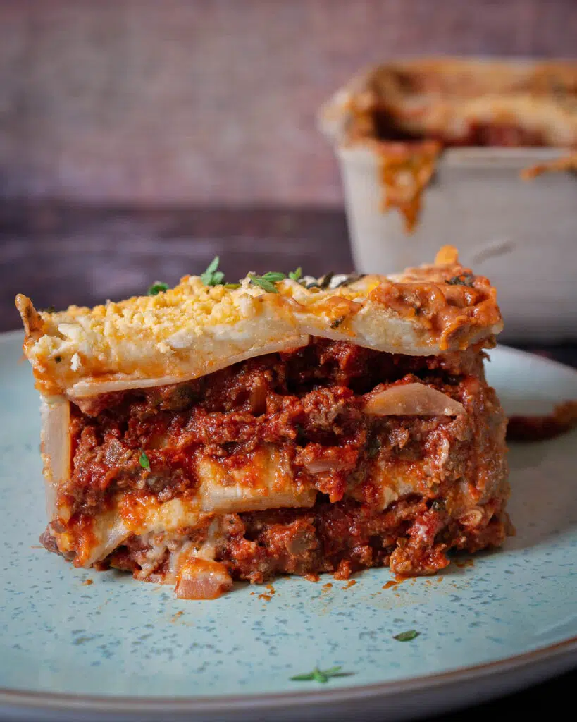 A slice of vegan potato gratin lasagne showing the layers of tomato mince, creamy gratin and a cheesy topping