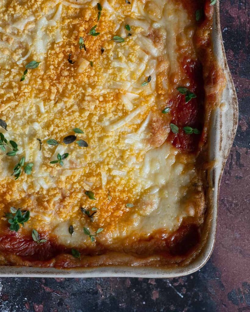 A baking dish filled with creamy vegan potato gratin lasagne, topped with vegan cheese and a sprinkling of fresh thyme