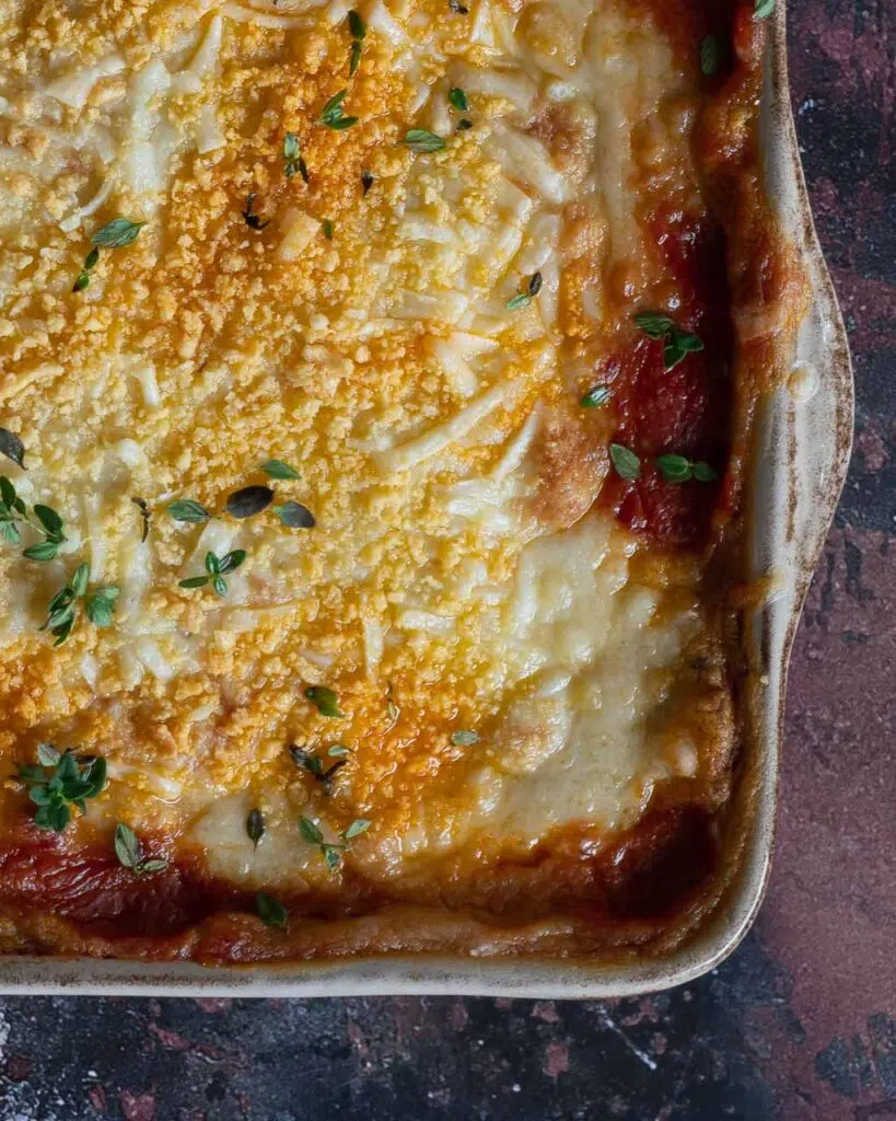 A baking dish filled with creamy vegan potato gratin lasagne, topped with vegan cheese and a sprinkling of fresh thyme