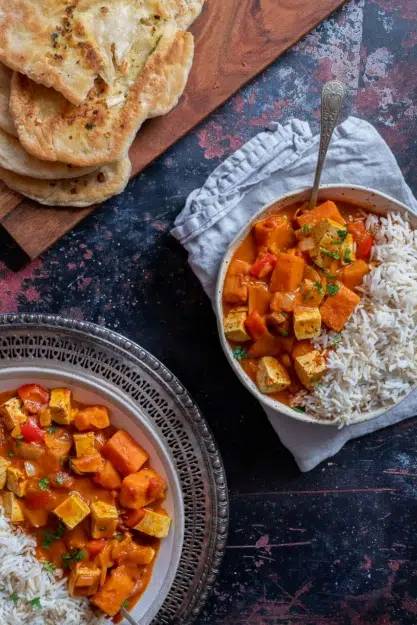 A top down shot of two bowls of rich orange vegan tikka masala served with white rice and naan bread