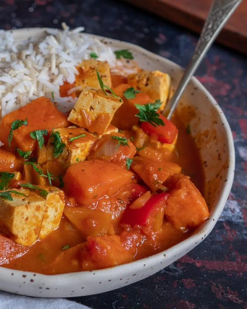 A bowl of rich orange vegan tikka masala served with white rice and naan bread