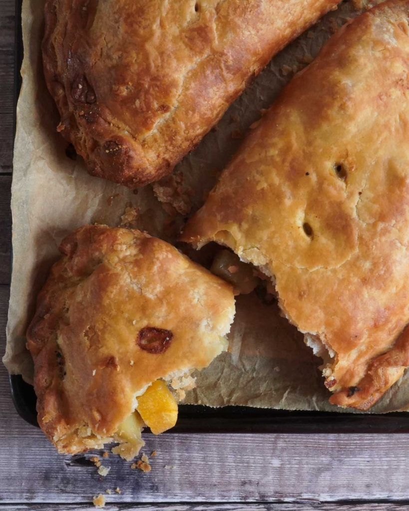 A golden, flaky, vegan Cornish pasty broken open on a baking tray