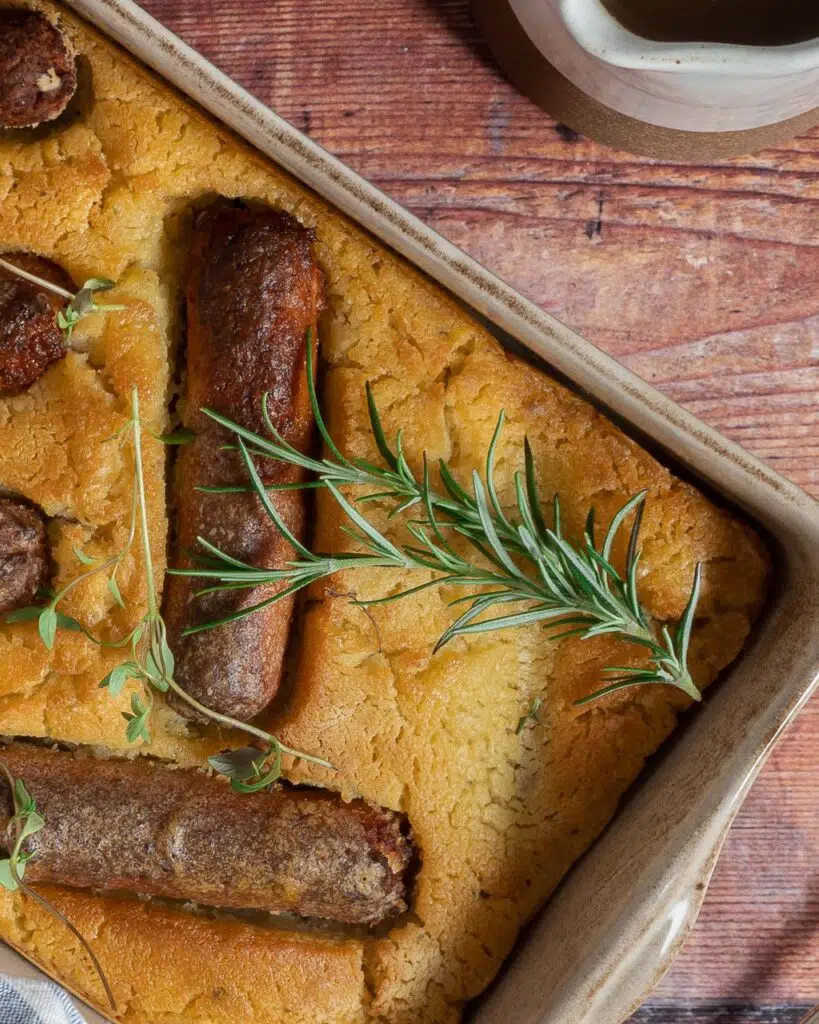 Vegan toad in the hole with crisp batter, golden sausages and fresh rosemary and thyme sprinkled on top