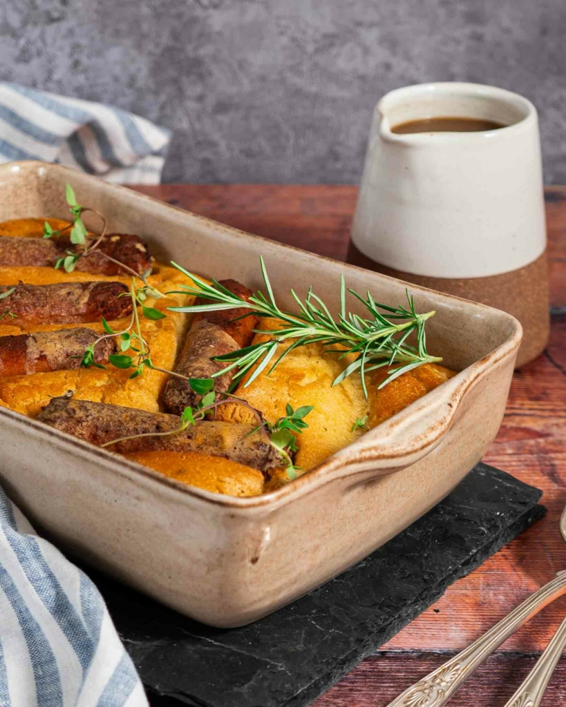 A baking dish filled with vegan toad in the hole, with a jug of gravy on the side