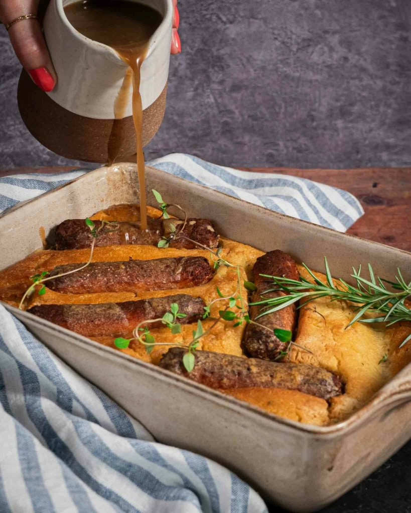 Gravy being poured onto a dish of golden, crisp vegan toad in the hole