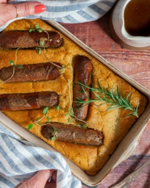 A dish of egg free toad in the hole with vegan sausages and fresh herbs