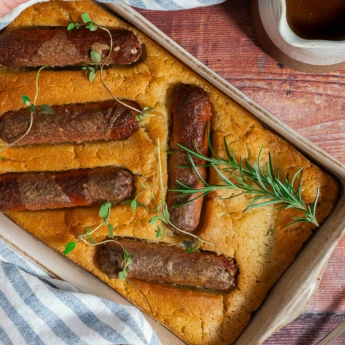 A dish of egg free toad in the hole with vegan sausages and fresh herbs