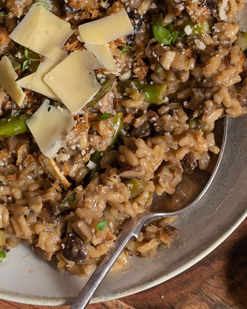 A bowl of creamy vegan mushroom and asparagus risotto topped with vegan parmesan and crispy fried onions