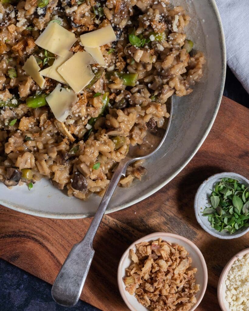 A bowl of creamy vegan mushroom and asparagus risotto topped with vegan parmesan and crispy fried onions
